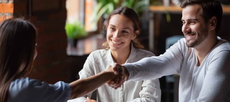 Young couple with man shaking hands to close on a mortgage