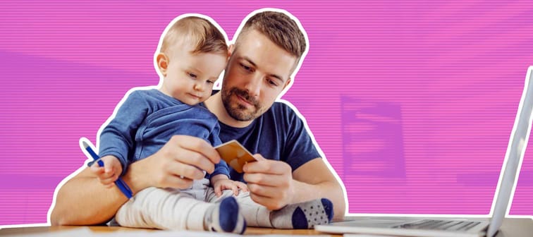 Young attractive bearded father sitting at dinning table with his beloved adorable son and paying bills online. His boy holding pen and trying to help him.